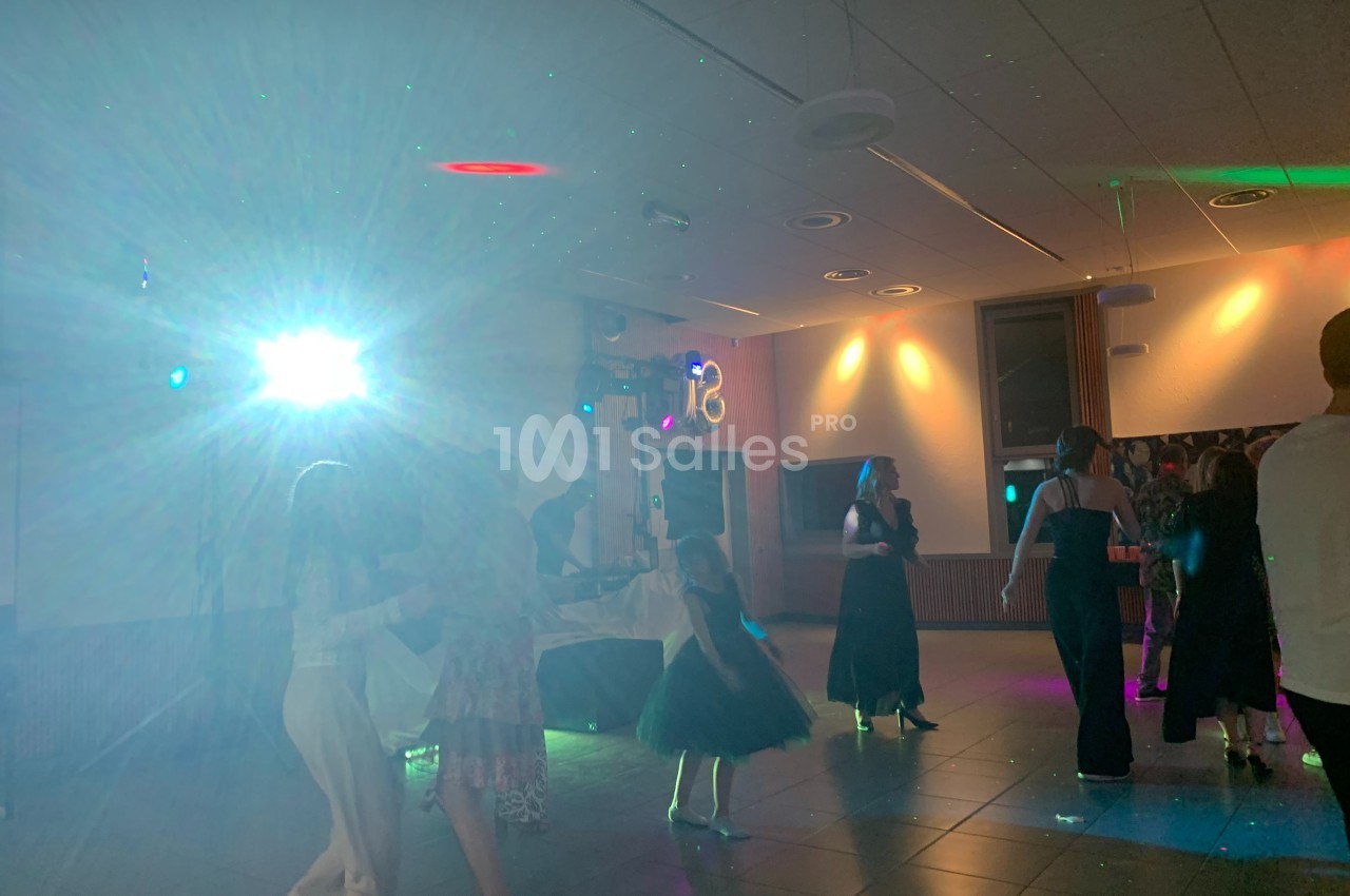 Des personnes dansent dans une salle éclairée par des lumières colorées et un projecteur lumineux.