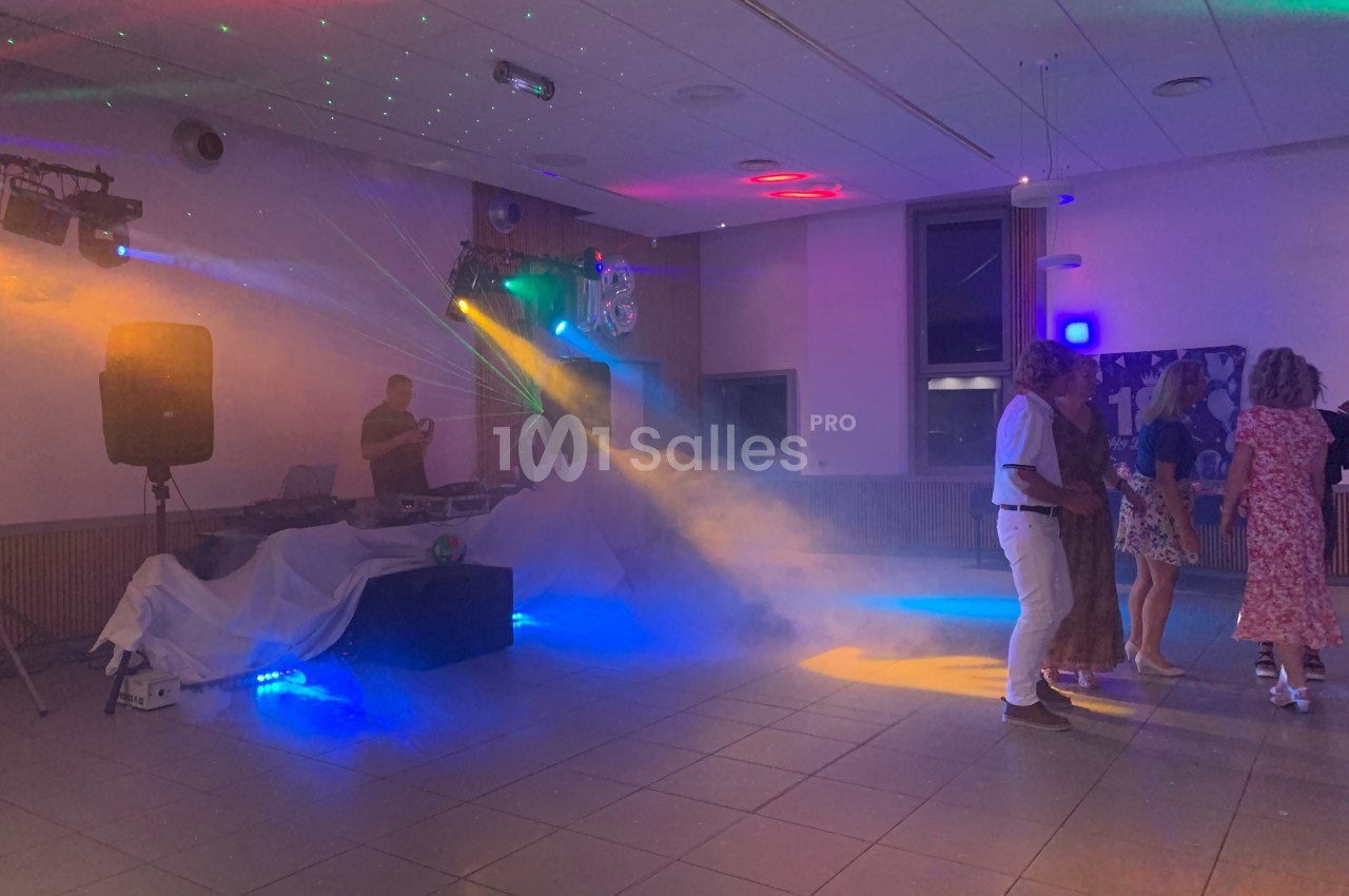 Personnes dansant dans une salle éclairée par des jeux de lumière colorés, avec un DJ en arrière-plan.