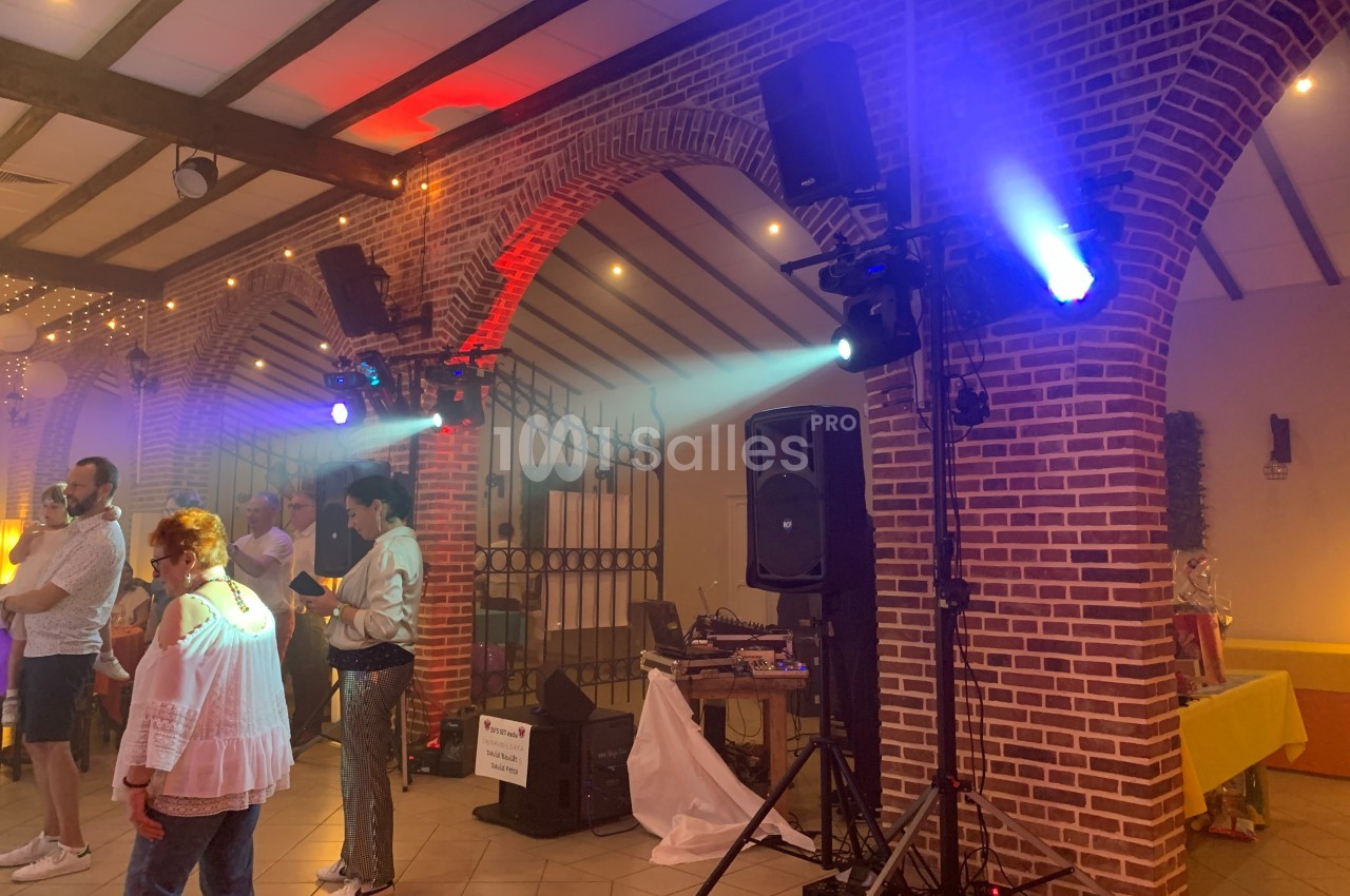 Salle de réception avec des invités debout, éclairages colorés et matériel de sonorisation près d'une arche en briques.