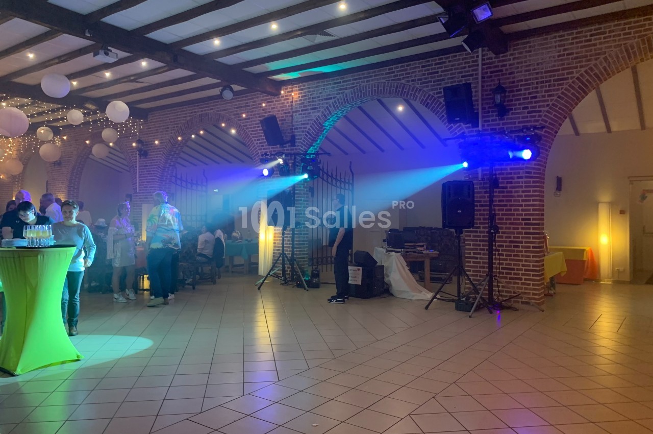 Salle de réception avec des invités debout, éclairages colorés et décorations suspendues.