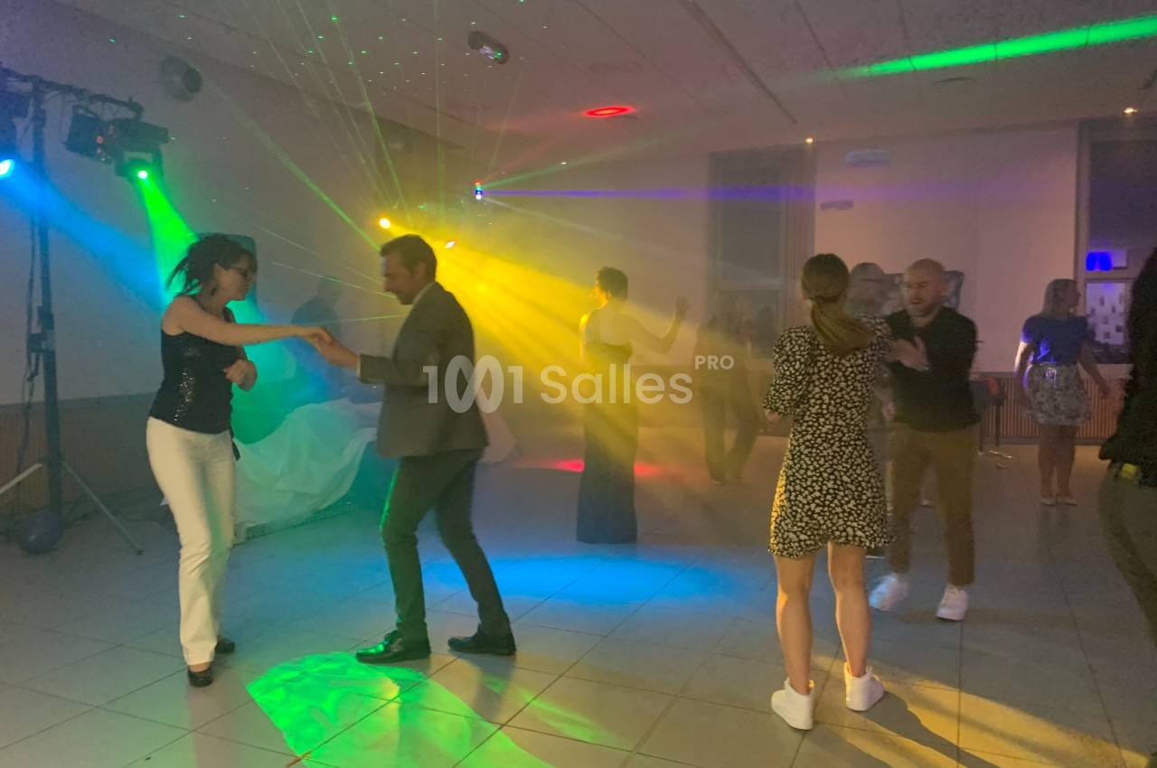 Des personnes dansent sous des lumières colorées dans une salle sombre lors d'une soirée festive.