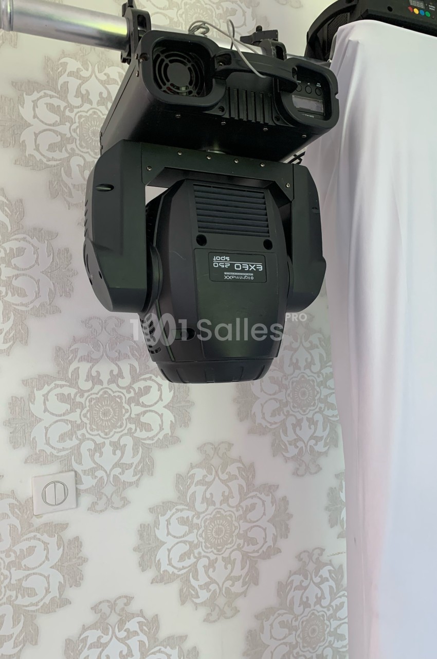 Projecteur d'éclairage suspendu à une structure métallique, devant un mur décoré de motifs floraux.