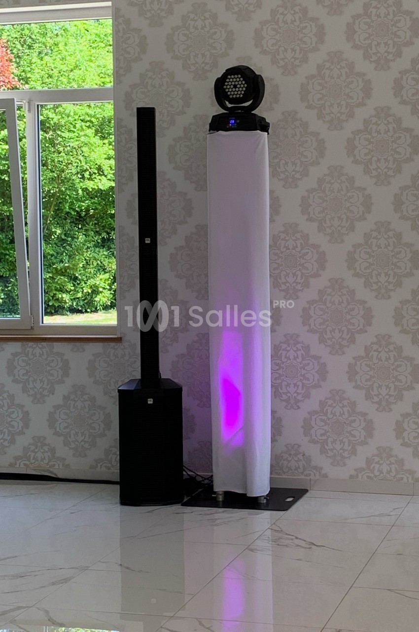 Colonne lumineuse avec éclairage violet et équipement audio à côté, installés dans une pièce lumineuse avec vue sur un…