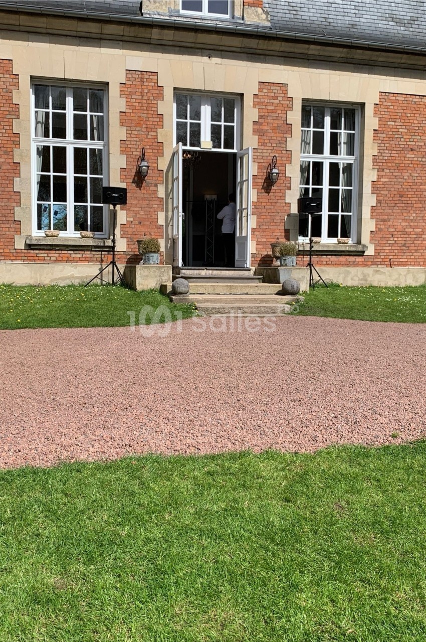 Façade d'un bâtiment en briques avec grandes fenêtres, porte ouverte et équipements audio installés à l'extérieur.