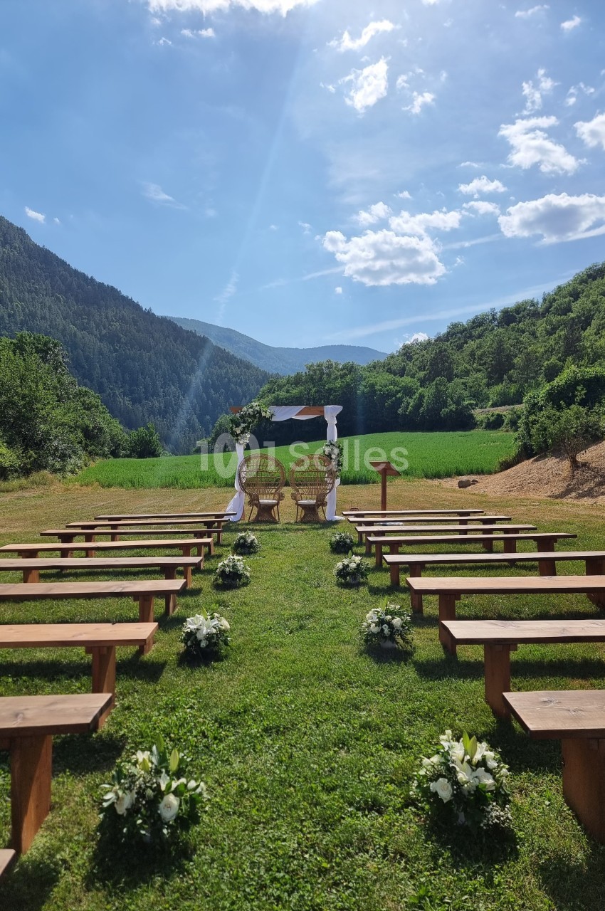 Allée bordée de bancs en bois menant à une arche décorée pour une cérémonie en plein air, entourée de montagnes verdoyantes.
