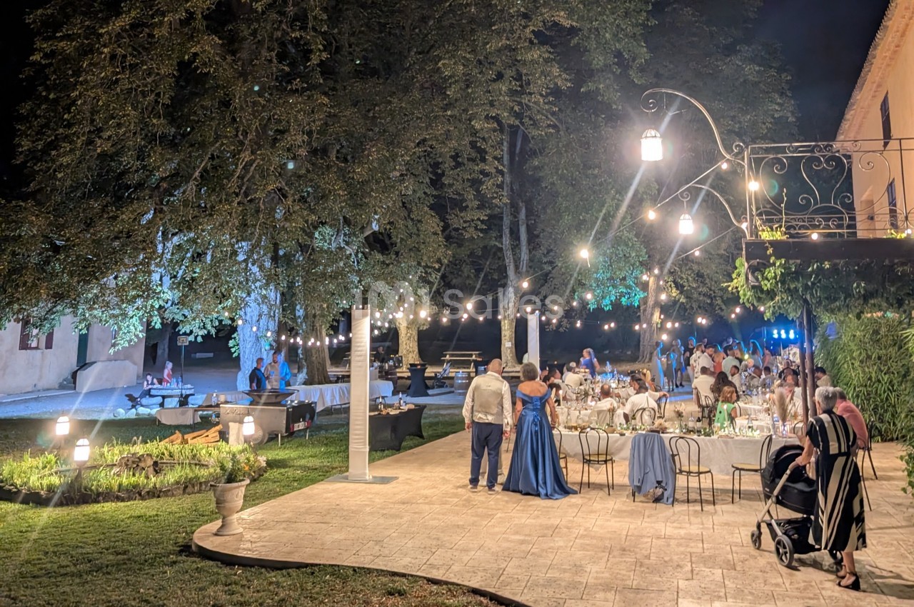 Dîner en plein air sous des guirlandes lumineuses, avec des invités élégants dans un jardin éclairé en soirée.