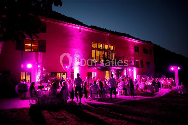 Groupe de personnes dînant en extérieur devant un bâtiment éclairé par des lumières roses, en soirée.