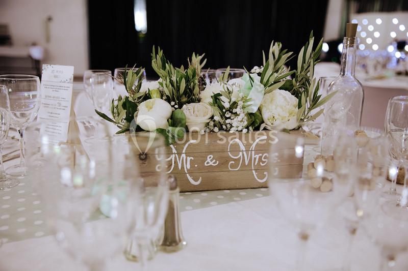 Centre de table avec fleurs blanches et feuillage dans une boîte en bois marquée ’Mr. & Mrs.’, entouré de verres.