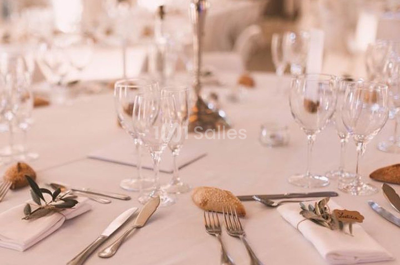 Table élégamment dressée avec nappes blanches, couverts alignés, verres à pied et décorations végétales.