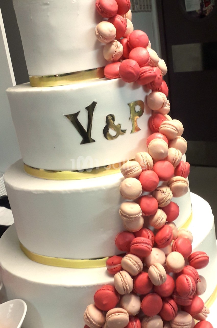 Gâteau de mariage à trois étages décoré de macarons roses et rouges, avec initiales dorées ’Y & P’.