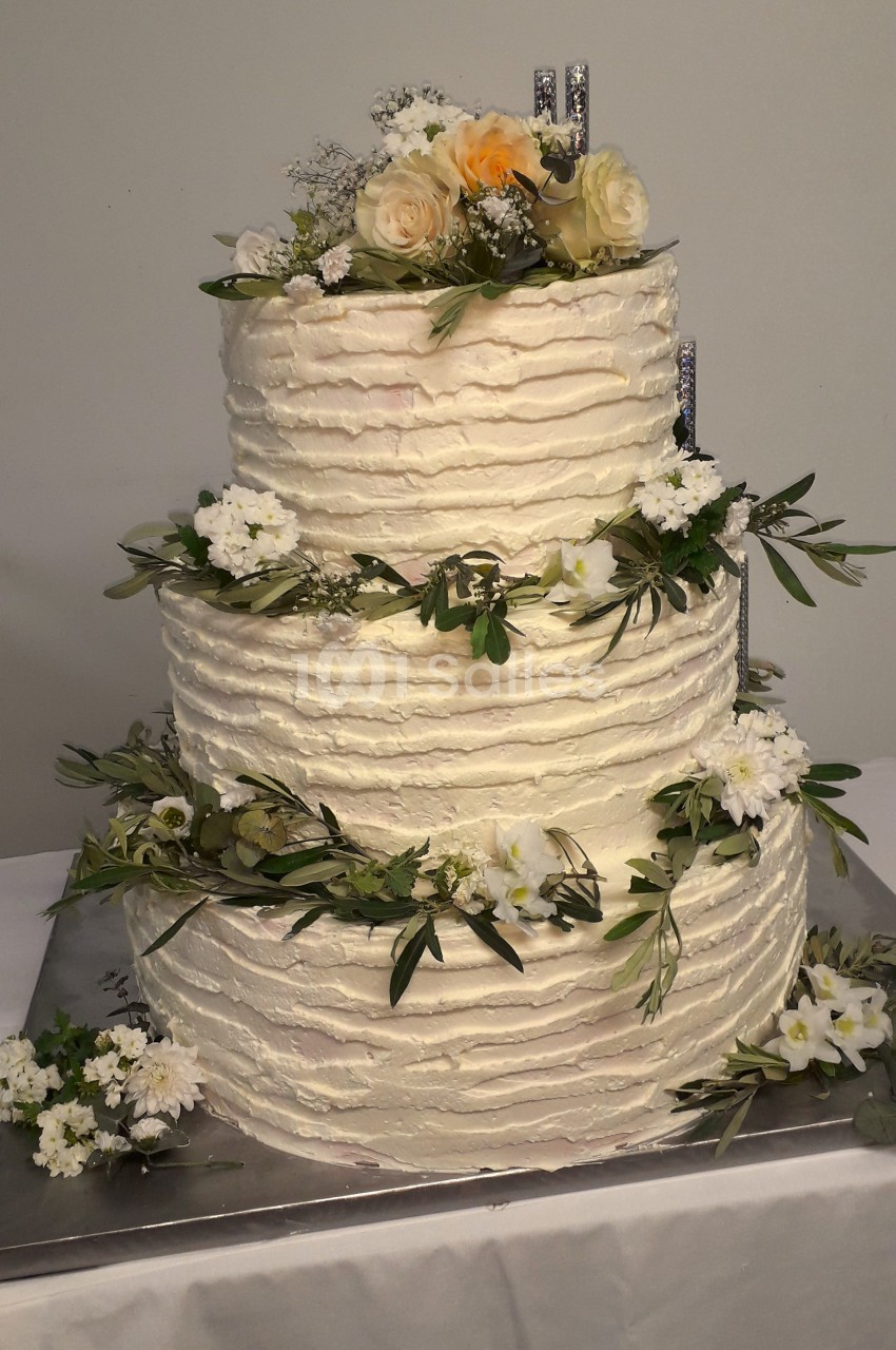 Gâteau de mariage à trois étages décoré de fleurs blanches, feuillages et roses crème au sommet.
