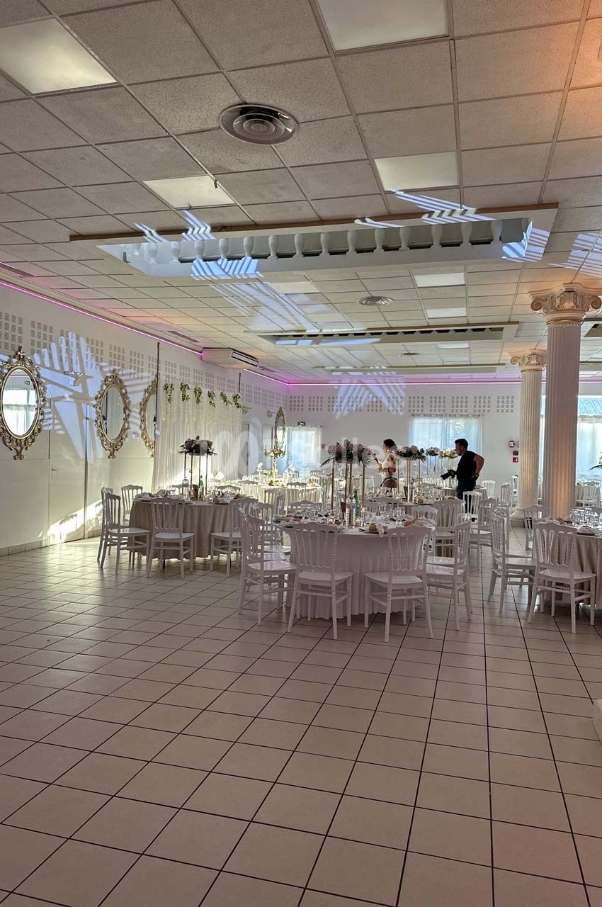 Salle de réception lumineuse avec tables décorées, chaises blanches et miroirs ornant les murs.