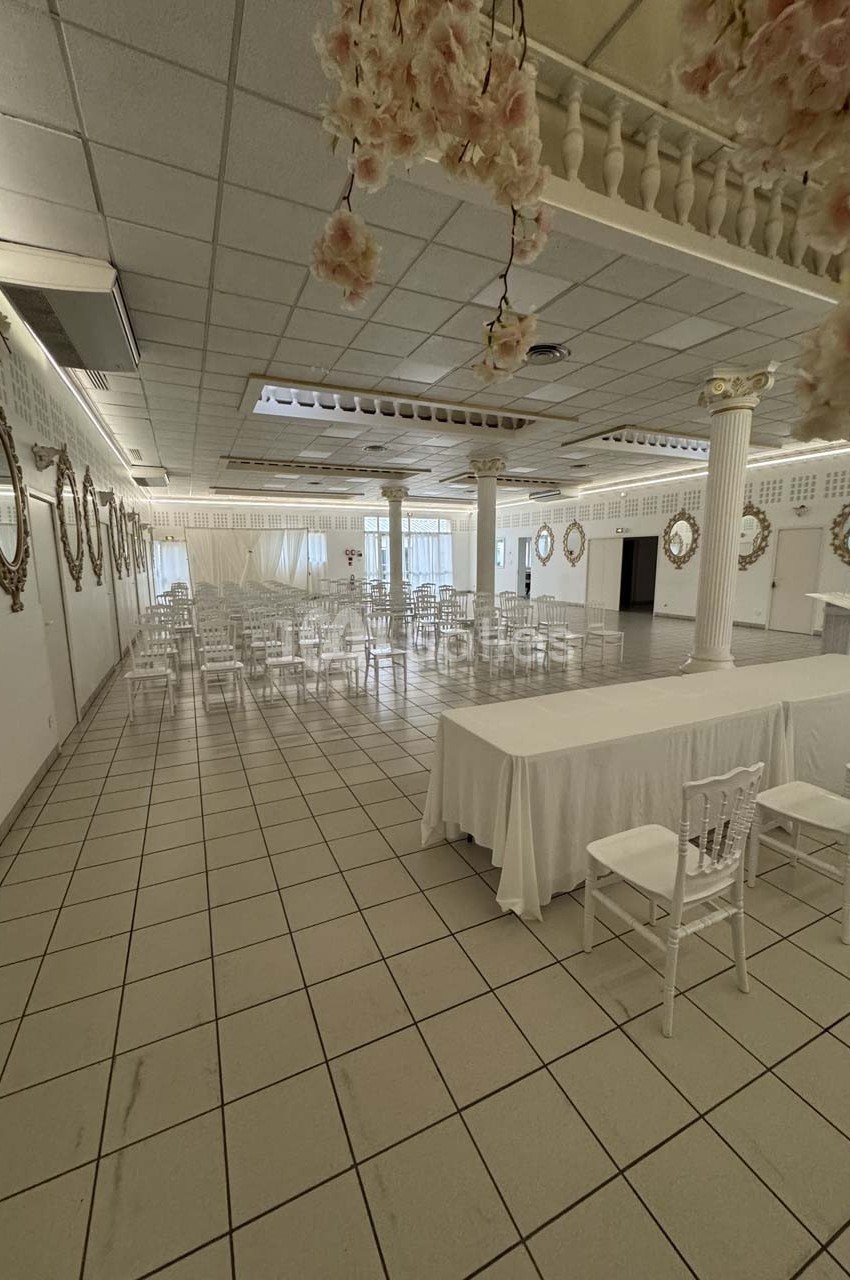 Salle de réception lumineuse avec tables et chaises blanches, décorée de colonnes et de miroirs muraux.