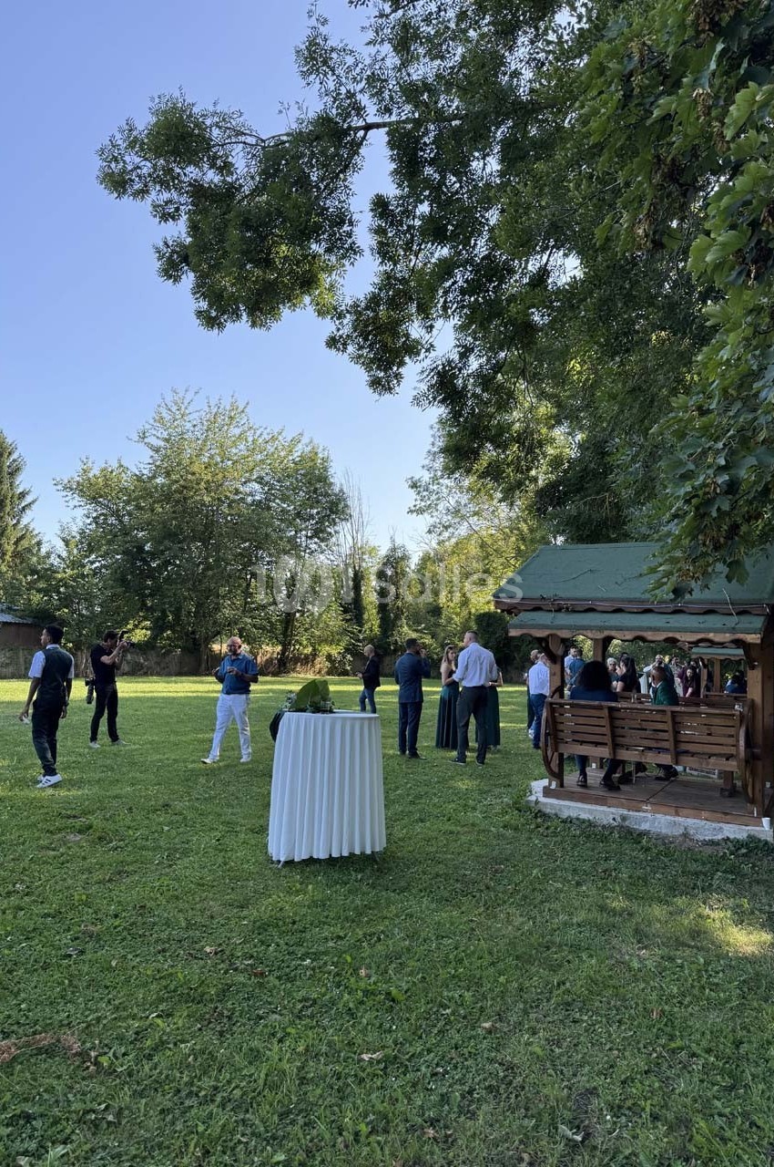 Un groupe de personnes discutant dans un jardin verdoyant avec une tonnelle en bois et une table haute en premier plan.