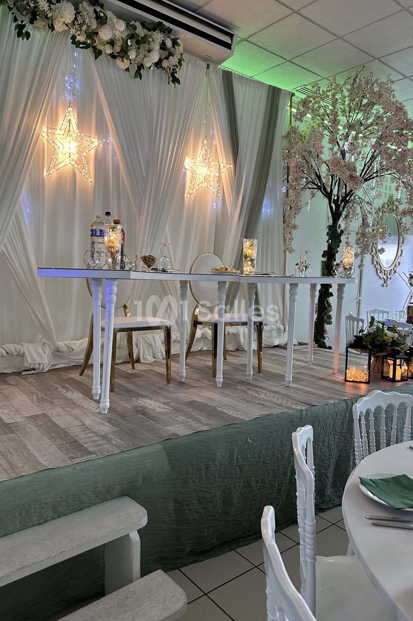 Table d'honneur décorée avec des fleurs, des étoiles lumineuses et des bougies, dans une salle de réception élégante.