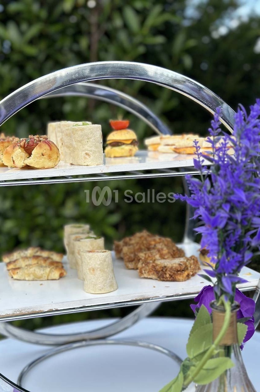 Plateau à étages avec des amuse-bouches variés, accompagné d'un bouquet de fleurs violettes au premier plan.