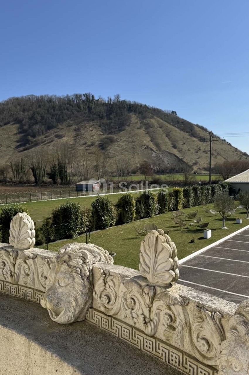 Vue d'une colline verdoyante sous un ciel bleu, avec un premier plan de balustrade ornée de sculptures.