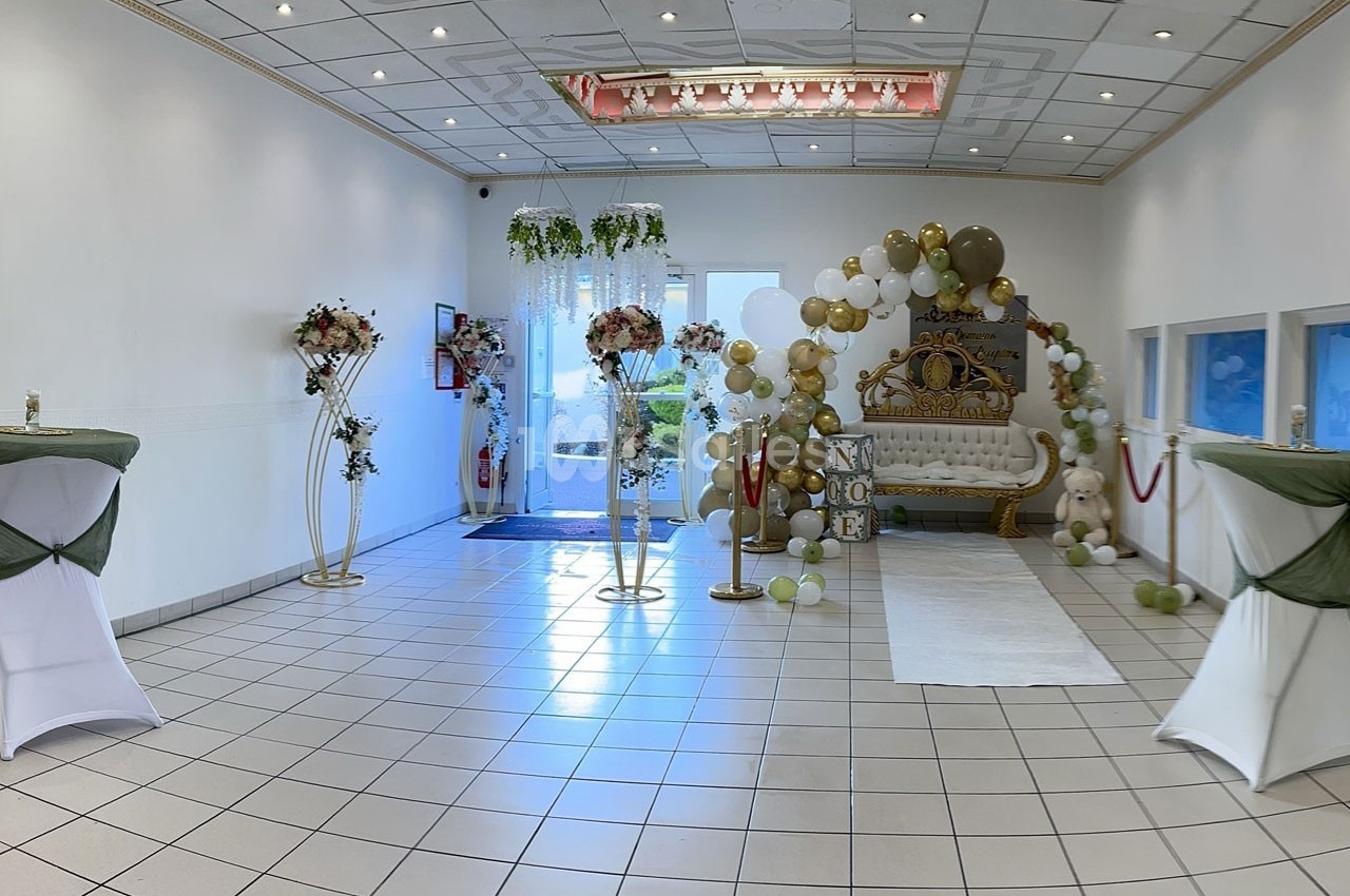 Salle décorée pour un événement avec arche de ballons, canapé doré, tables hautes et fleurs.
