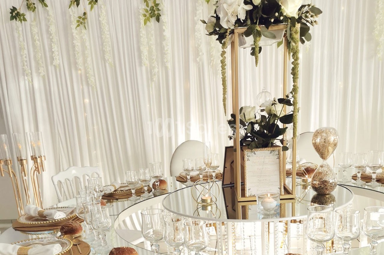 Table élégamment dressée avec vaisselle raffinée, centre de table floral et décoration lumineuse en arrière-plan.