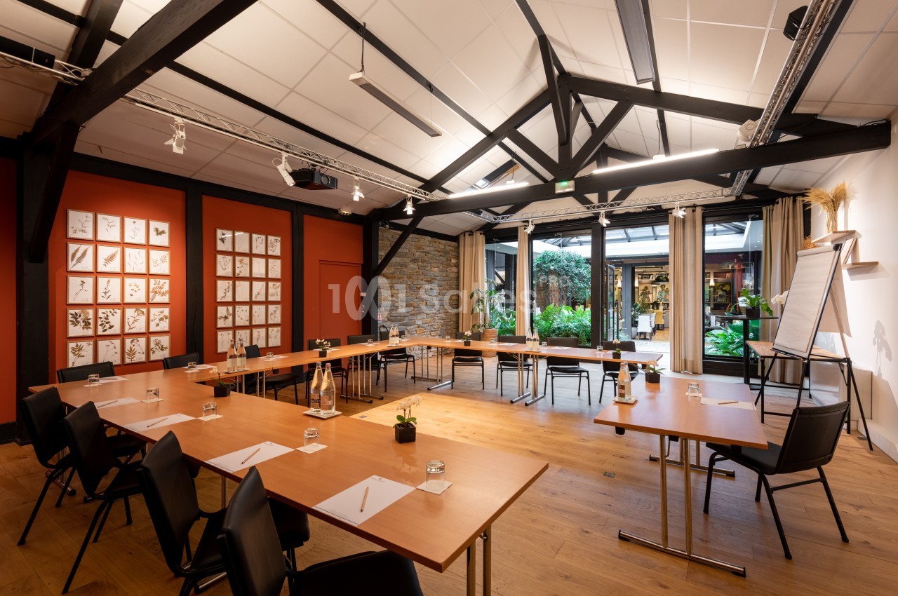 Salle de réunion lumineuse avec tables en U, chaises noires, murs décorés et vue sur un jardin extérieur.
