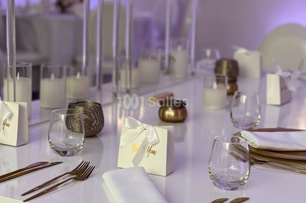 Table élégamment dressée avec couverts, verres, bougies et boîtes cadeaux blanches ornées de rubans.