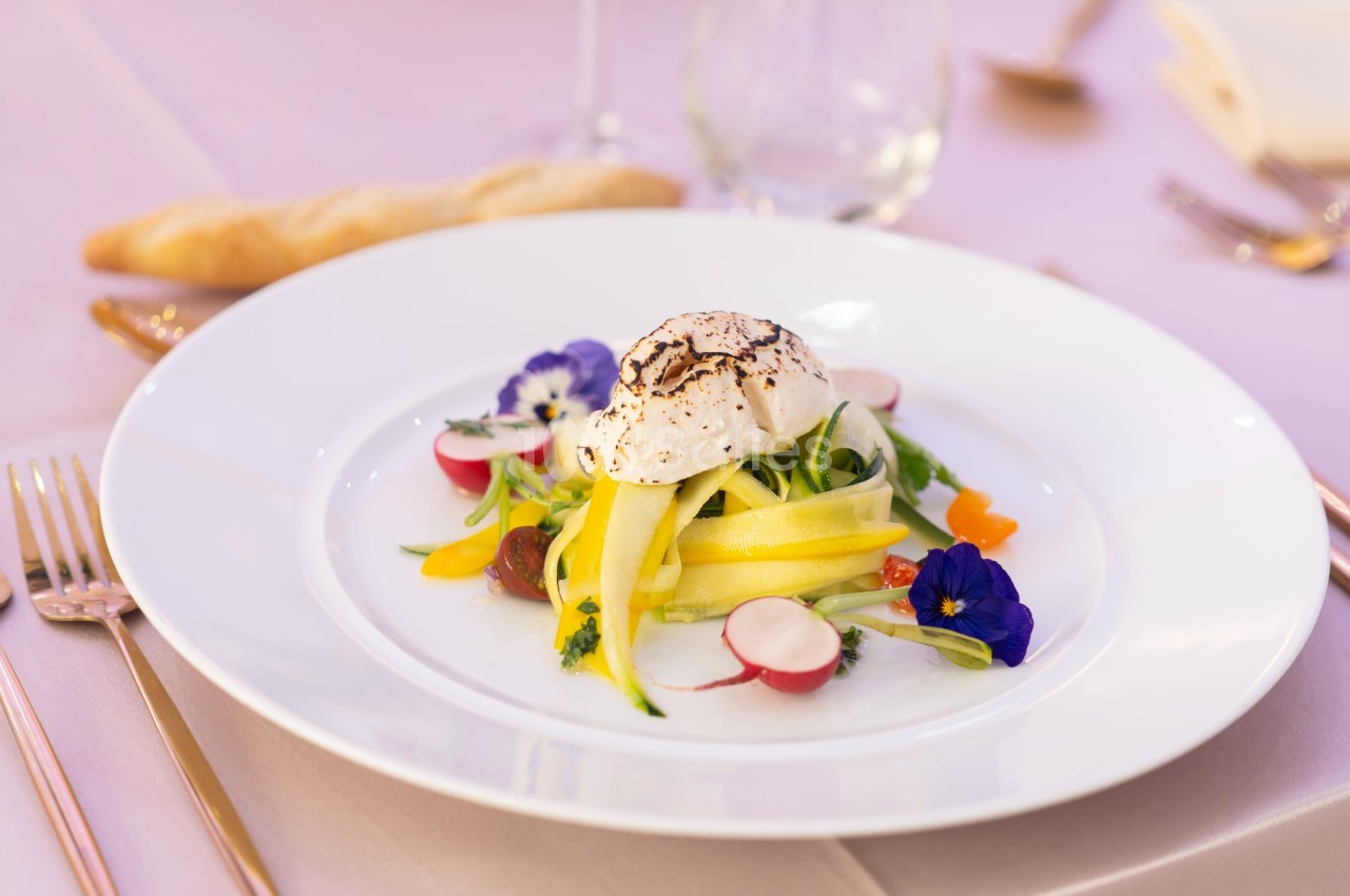Assiette de légumes colorés avec une quenelle de fromage, décorée de fleurs comestibles, sur une table élégante.