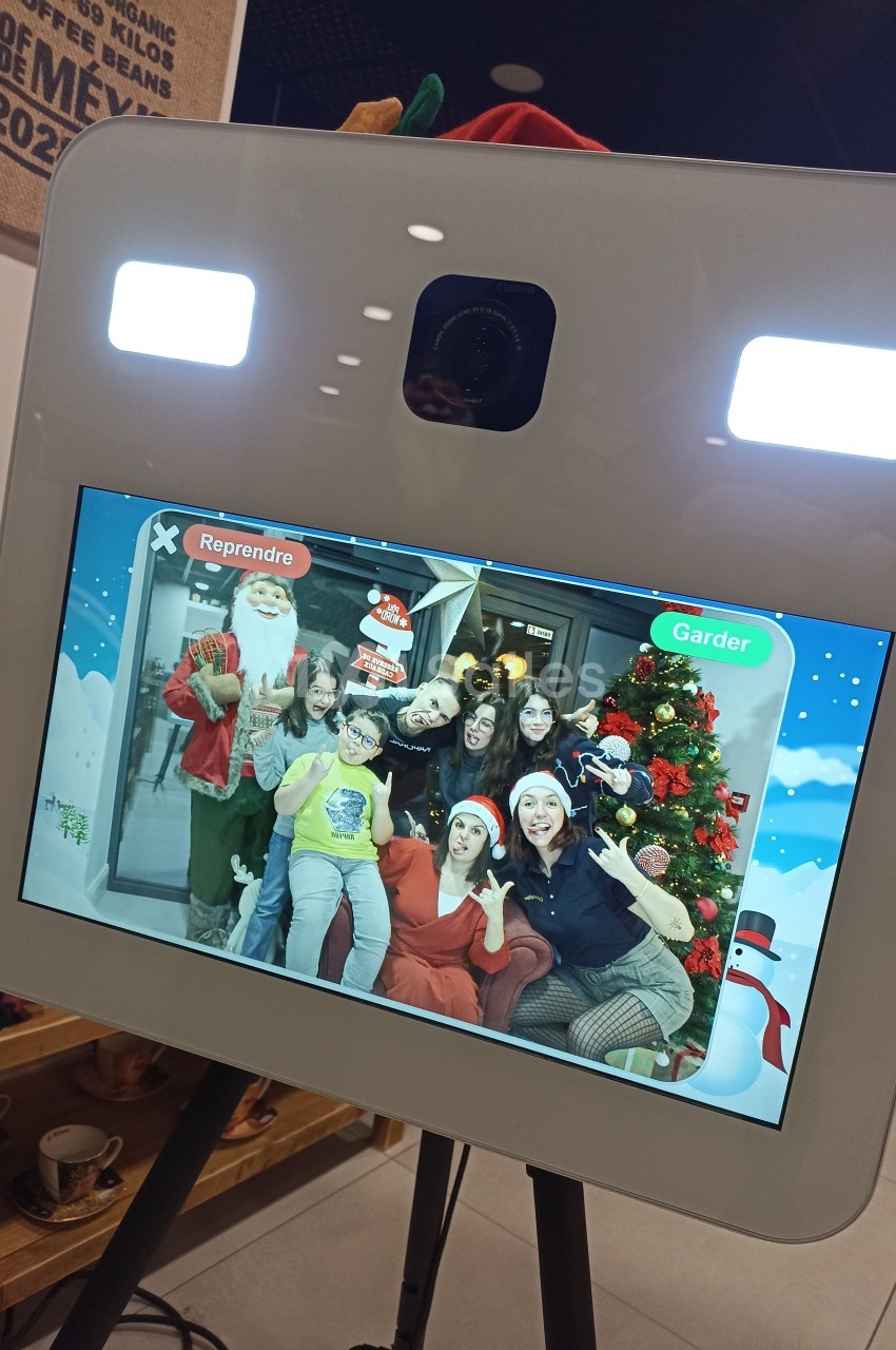 Des personnes souriantes posent devant un écran de photobooth avec des décorations de Noël en arrière-plan.
