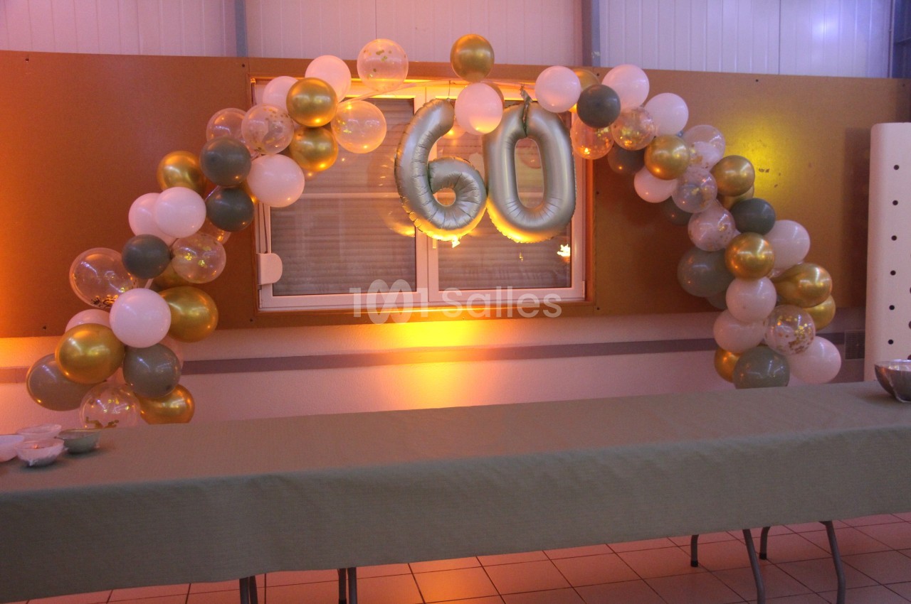 Décoration d'anniversaire avec arche de ballons dorés, blancs et verts, et le chiffre 60 en ballons argentés.
