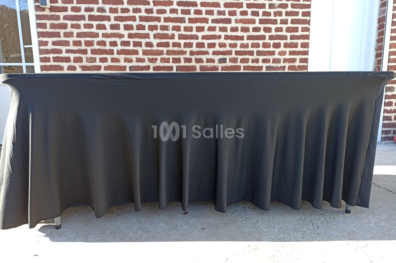 Table recouverte d'une nappe noire plissée, placée devant un mur de briques rouges et une porte blanche.