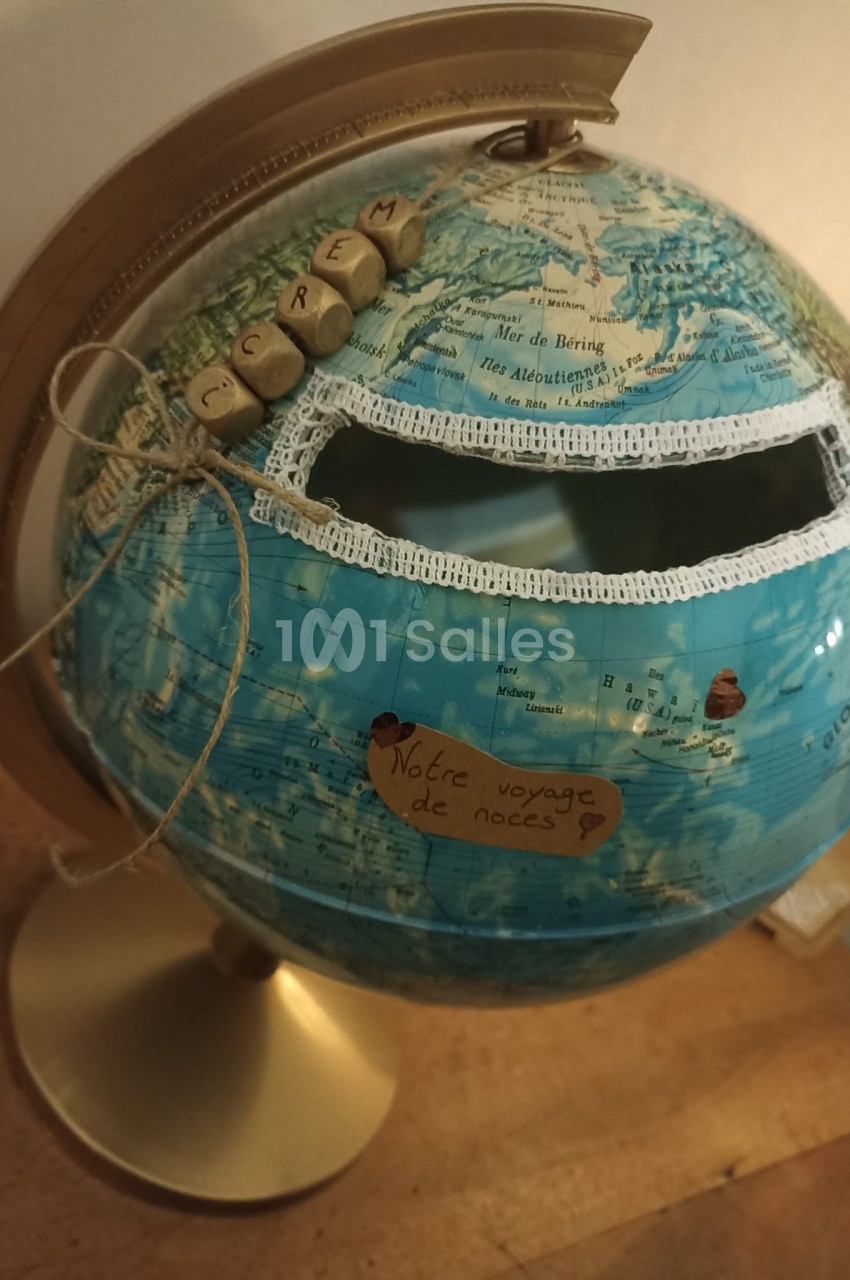 Globe terrestre transformé en urne avec une fente décorée et une étiquette indiquant ’Notre voyage de noces’.