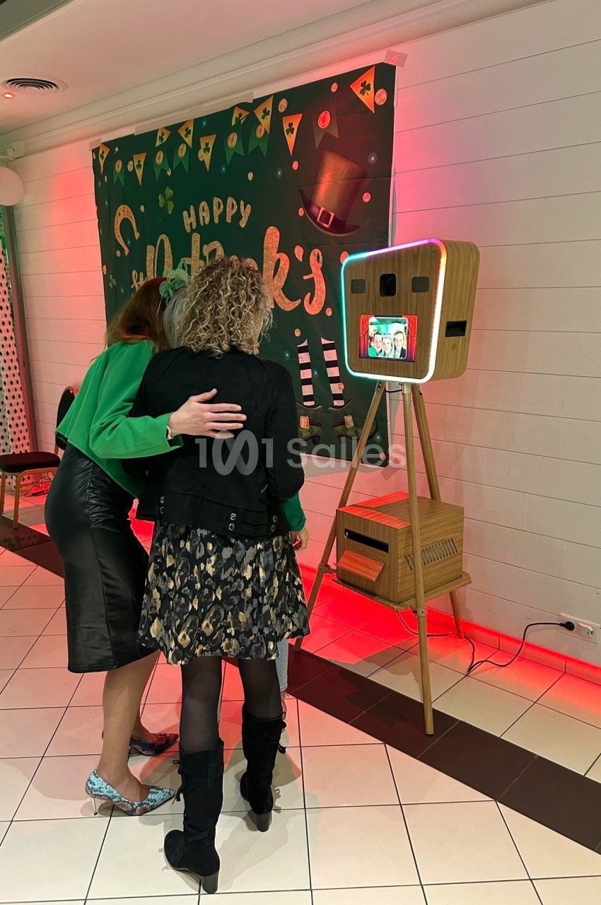 Deux femmes regardent un écran d'une borne photo rétro dans un espace décoré pour la Saint-Patrick.