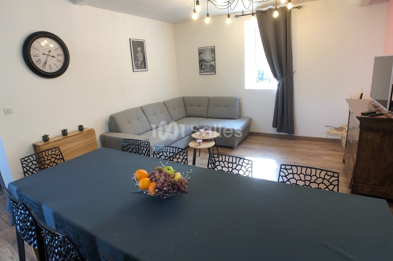 Salle à manger avec une grande table, un canapé d'angle, un luminaire suspendu et une décoration sobre.