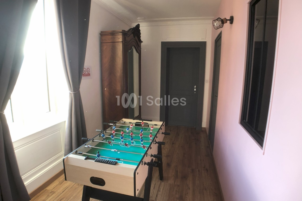 Table de baby-foot dans une pièce lumineuse avec parquet, murs roses et un grand miroir en bois.