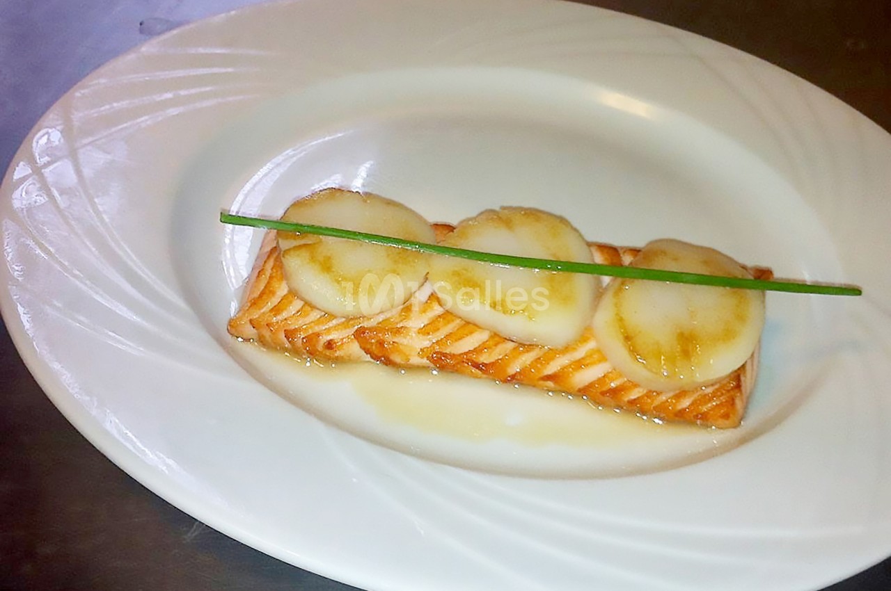 Filet de saumon grillé garni de tranches de Saint-Jacques et d'une tige de ciboulette, présenté sur une assiette blanche.