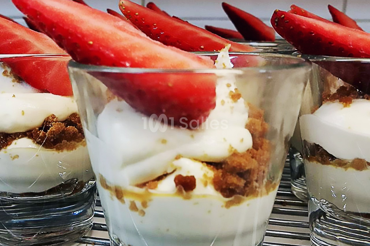 Verrines de dessert composées de crème, miettes de biscuit et morceaux de fraises fraîches en garniture.