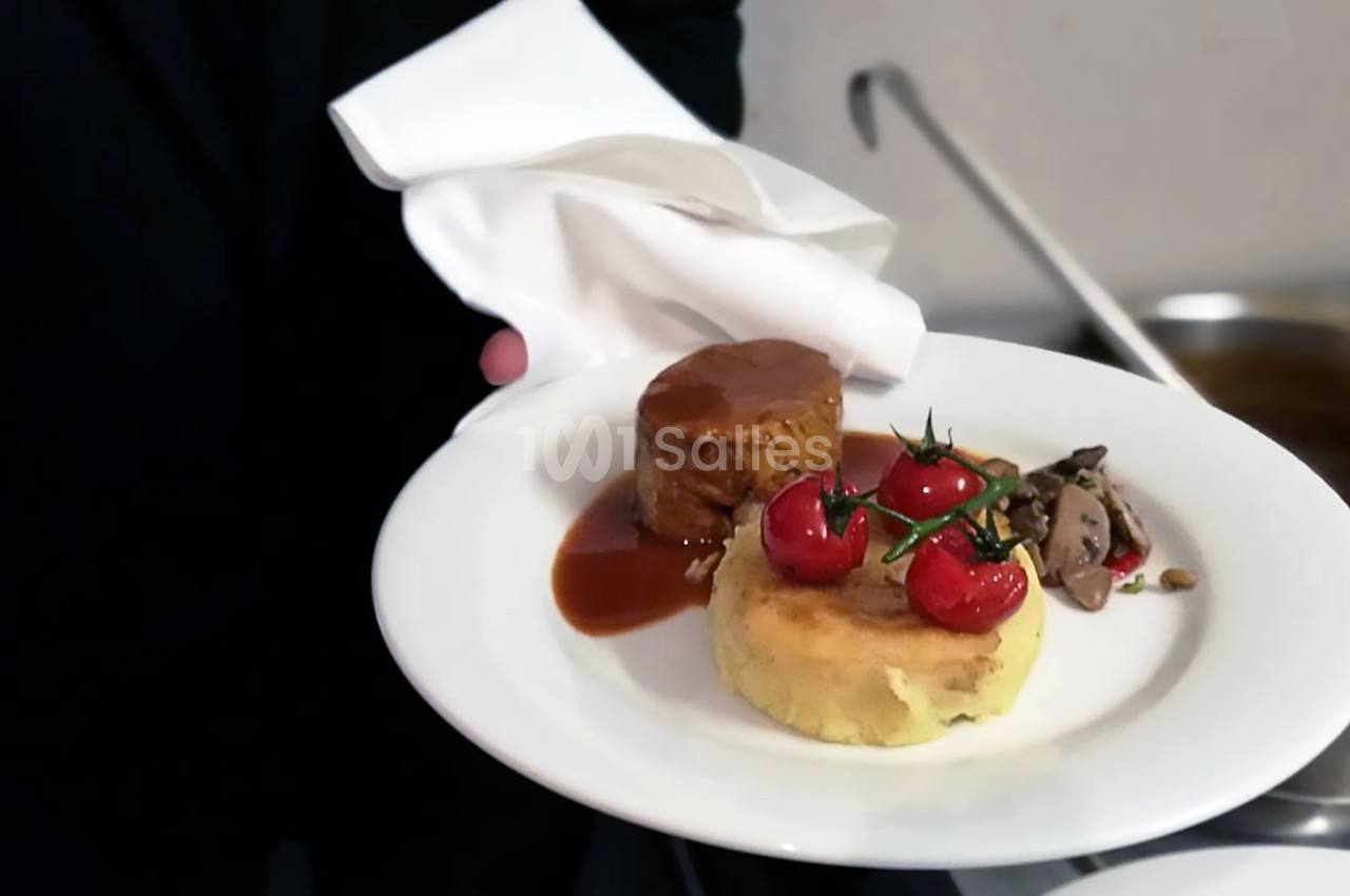 Assiette contenant un filet de viande nappé de sauce, une purée garnie de tomates cerises et des légumes sautés.