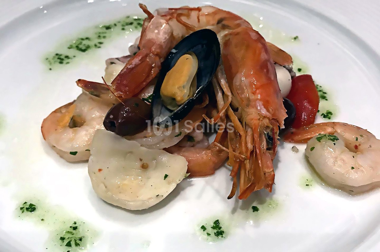 Assiette de fruits de mer avec crevettes, moules, calamars, tomates et herbes sur un lit de sauce verte.