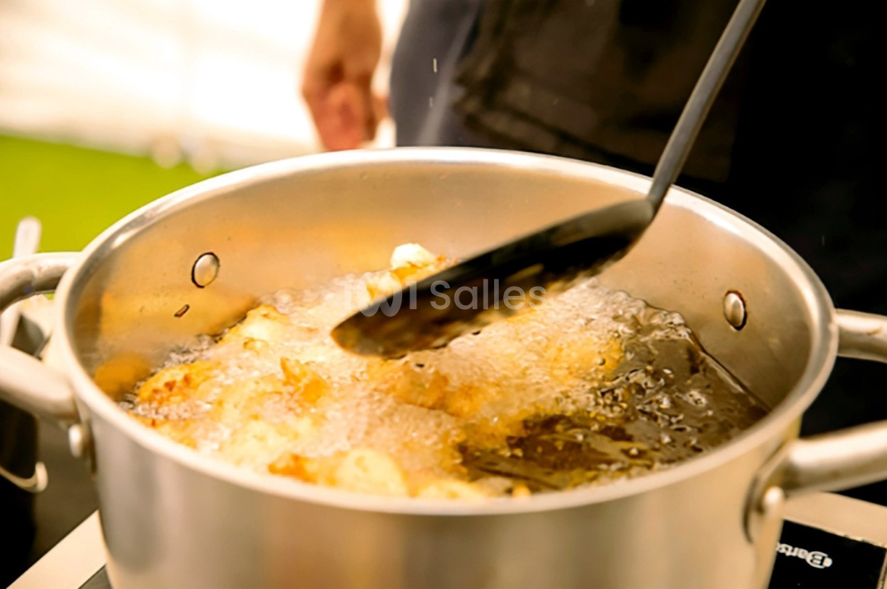 Cuisson de morceaux d'aliments frits dans une casserole d'huile bouillante, avec une écumoire en action.