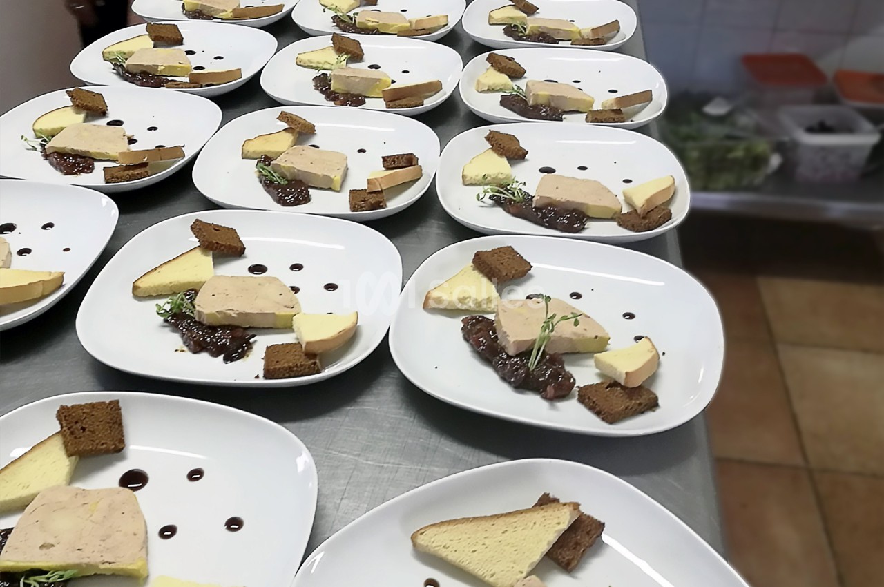 Assiettes dressées avec du foie gras, pain, confiture et décorations, alignées sur une table en cuisine.