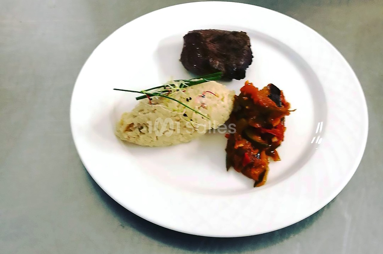 Assiette contenant un morceau de viande, une portion de risotto garni de ciboulette et des légumes mijotés.