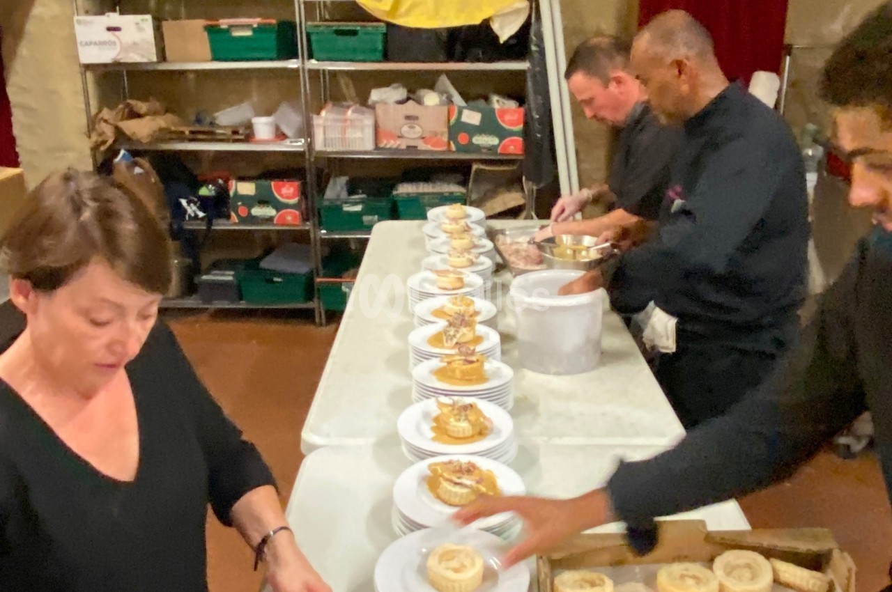 Des personnes préparent et disposent des desserts sur des assiettes alignées dans une cuisine professionnelle.