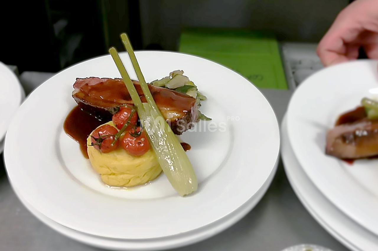Assiette gastronomique composée de viande, purée, légumes et sauce, présentée sur une table de service.