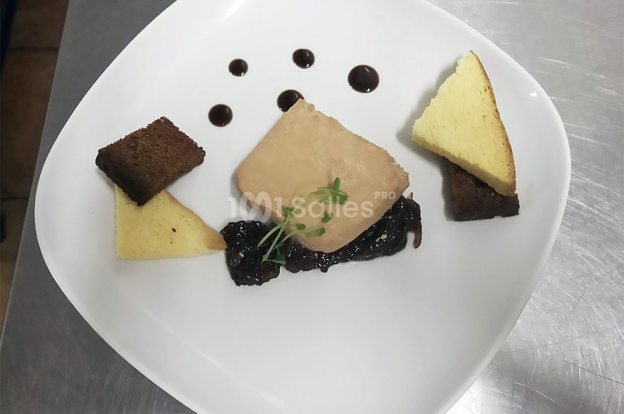 Assiette de foie gras avec pain brioché, pain d'épices, confiture et décor de sauce balsamique.