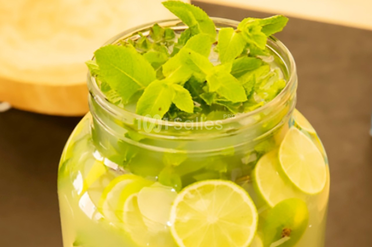Bocal en verre rempli d'eau infusée avec des tranches de citron vert et des feuilles de menthe fraîche.