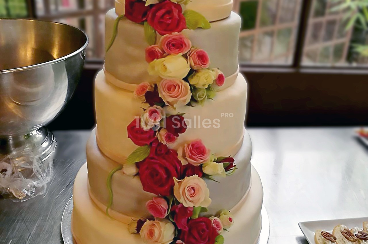 Gâteau de mariage à quatre étages décoré de roses rouges, roses et blanches, posé sur une table en métal.