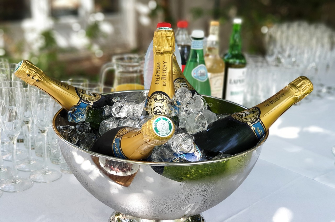 Seau en métal rempli de glace contenant plusieurs bouteilles de champagne, entouré de verres et de boissons.