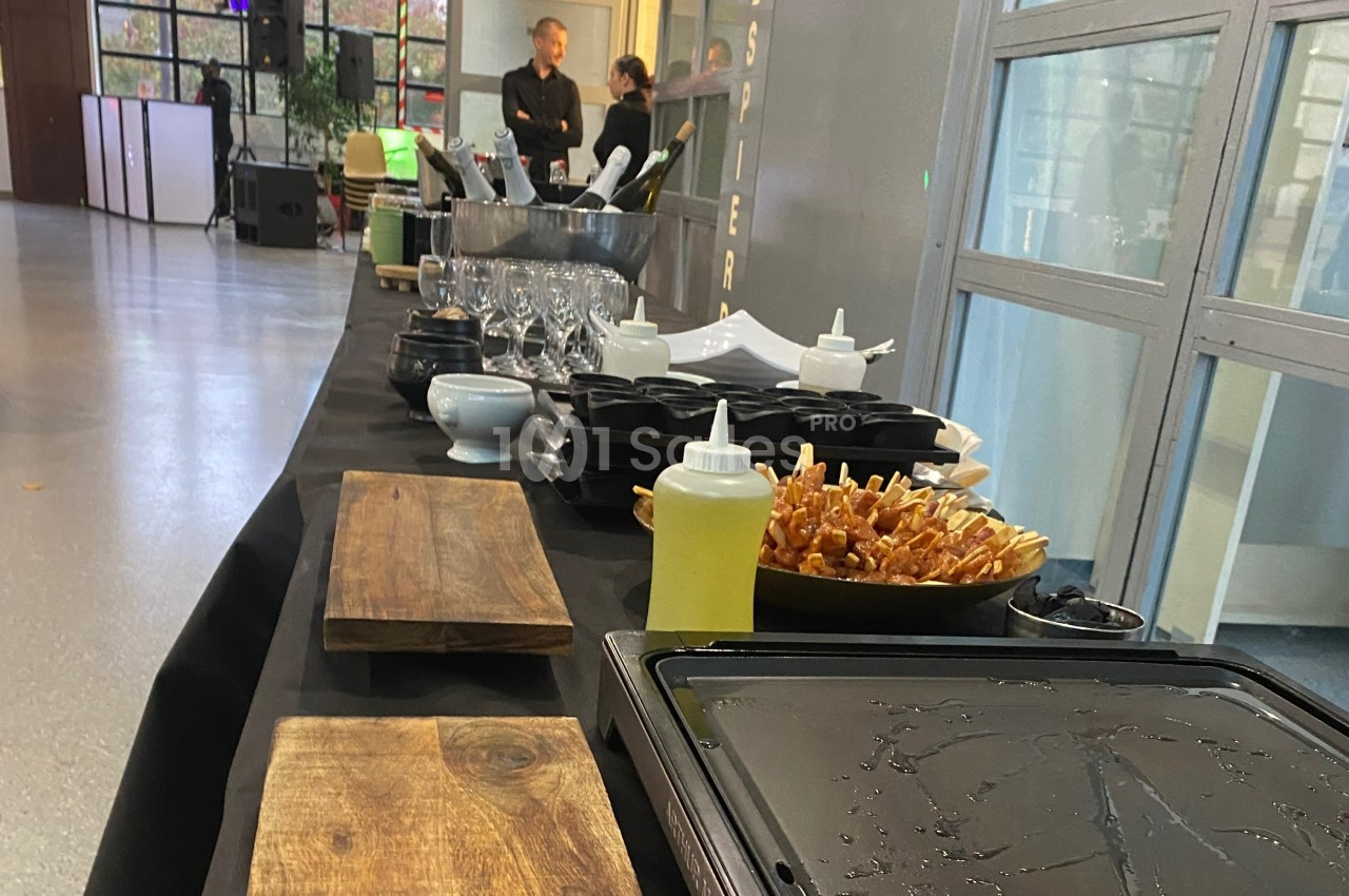 Table de buffet avec planches en bois, verrerie, condiments et brochettes disposées dans un espace intérieur lumineux.