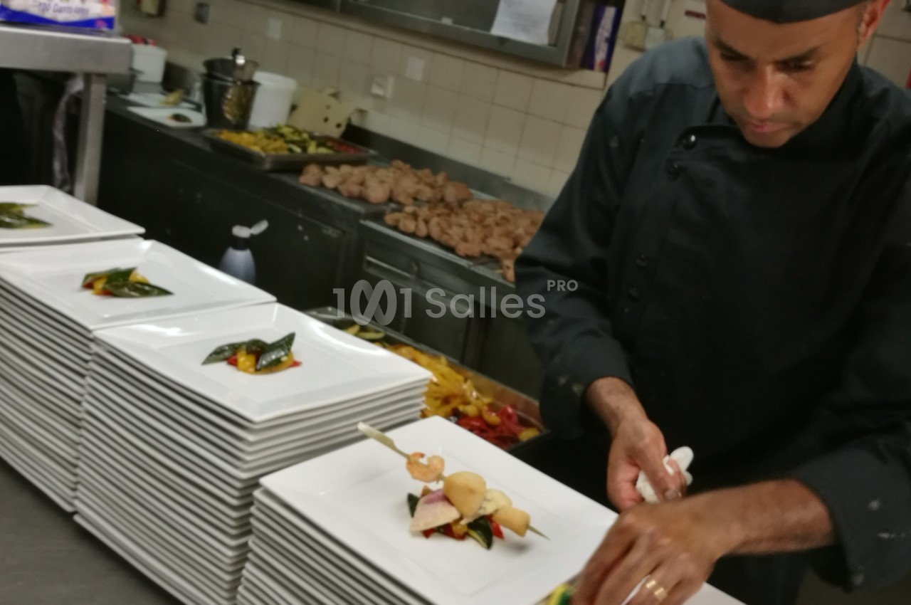 Un chef en cuisine dispose des assiettes garnies de plats soigneusement dressés sur un plan de travail.