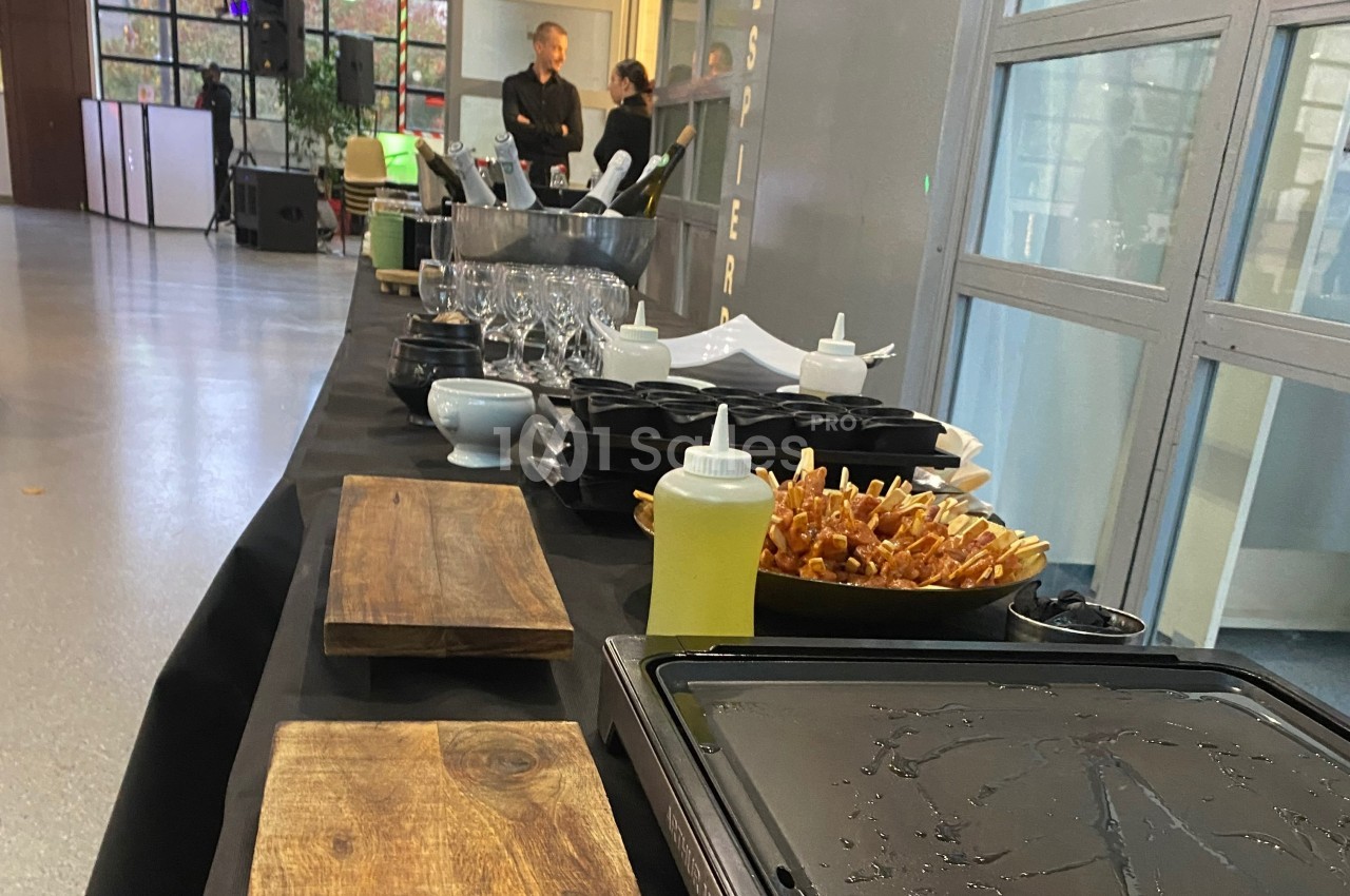 Table de buffet avec planches en bois, verrerie, condiments et plats préparés dans un espace intérieur lumineux.