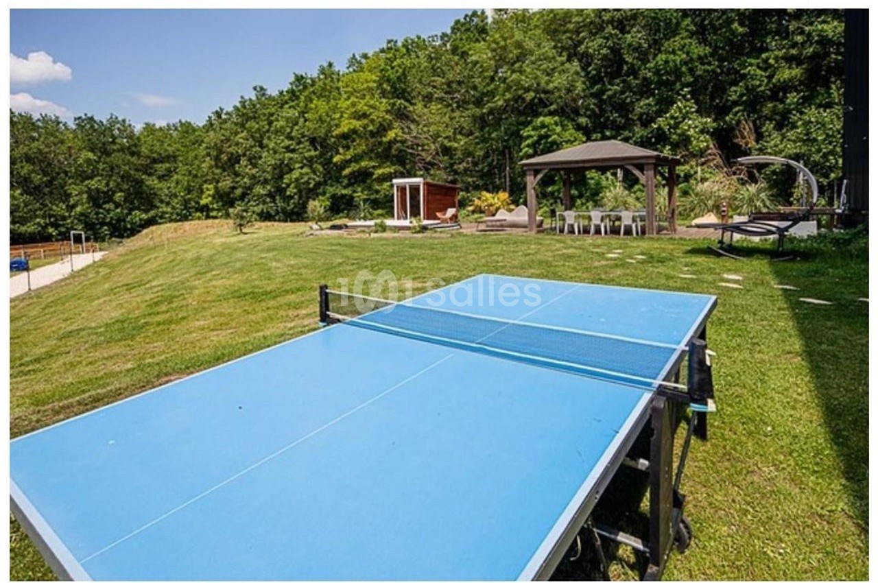 Table de ping-pong bleue installée sur une pelouse, avec un kiosque et des arbres en arrière-plan.